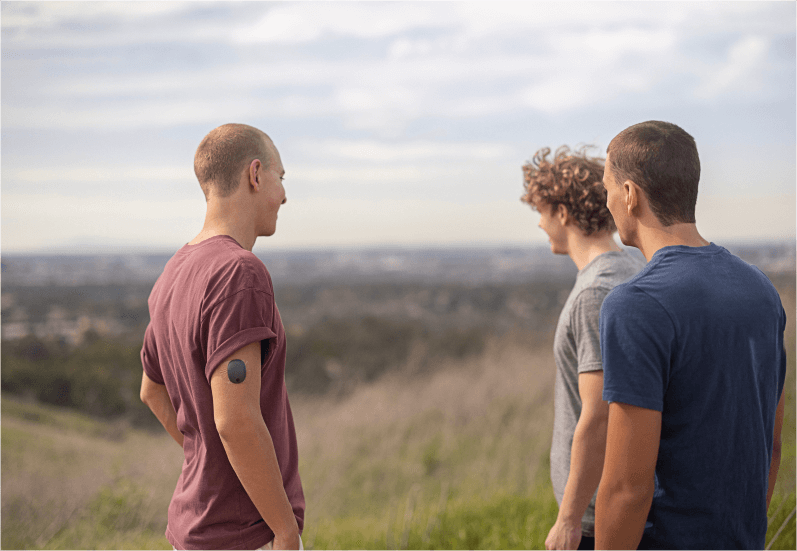 3 friends standing outside in field with one wearing Eversense CGM transmitter